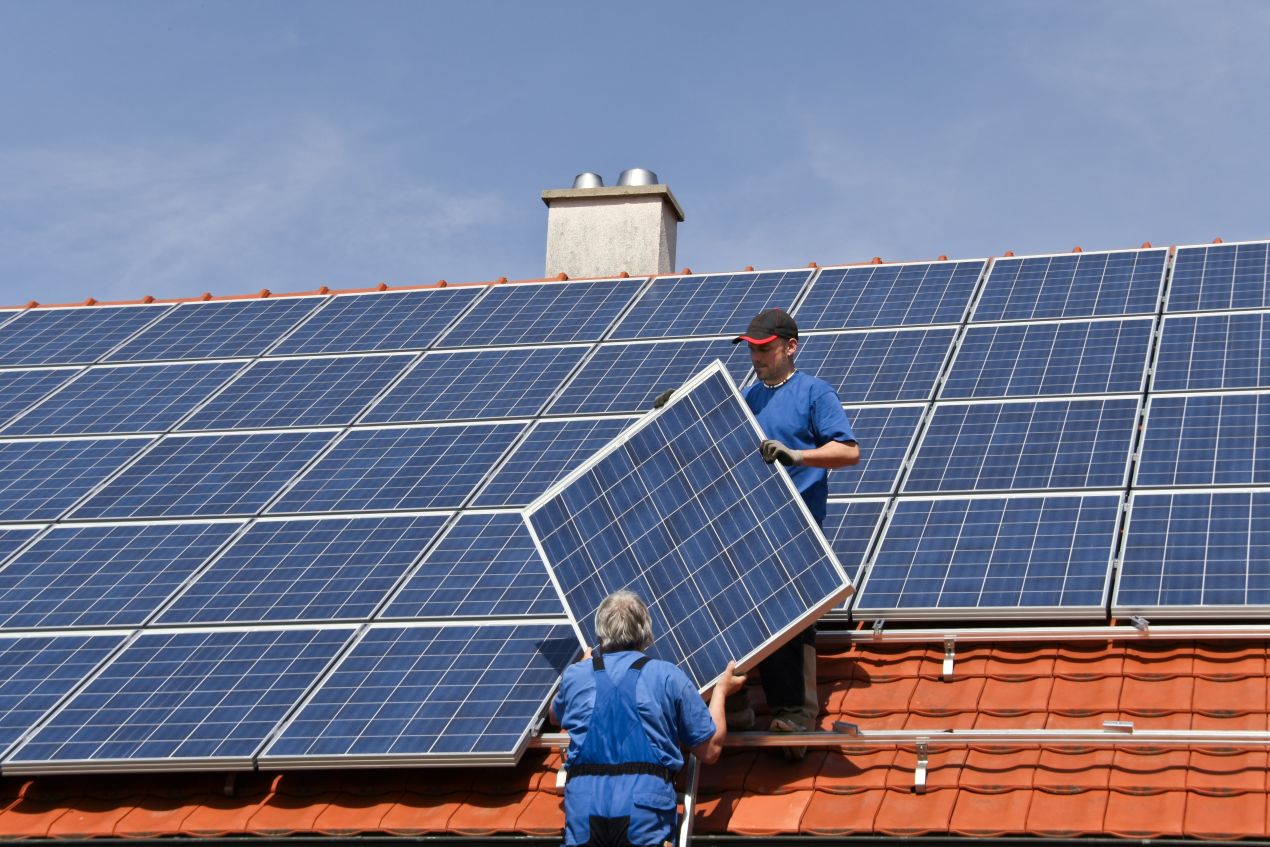 Zwei Monteure installieren ein Solarmodul auf einem Ziegeldach, typische Situation für die Anwendung von Komponenten aus dem Solar Grosshandel