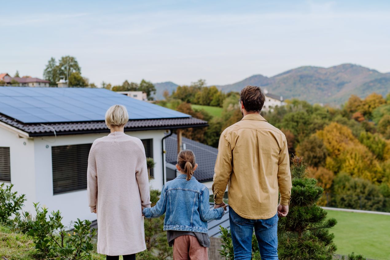 Familie mit Blick auf Haus mit Photovoltaikanlage in grüner Umgebung, Symbol für energieeffiziente Lösungen aus dem Solar Grosshandel